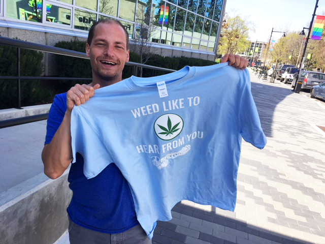 Man holding up shirt that reads "Weed need to hear from you"
